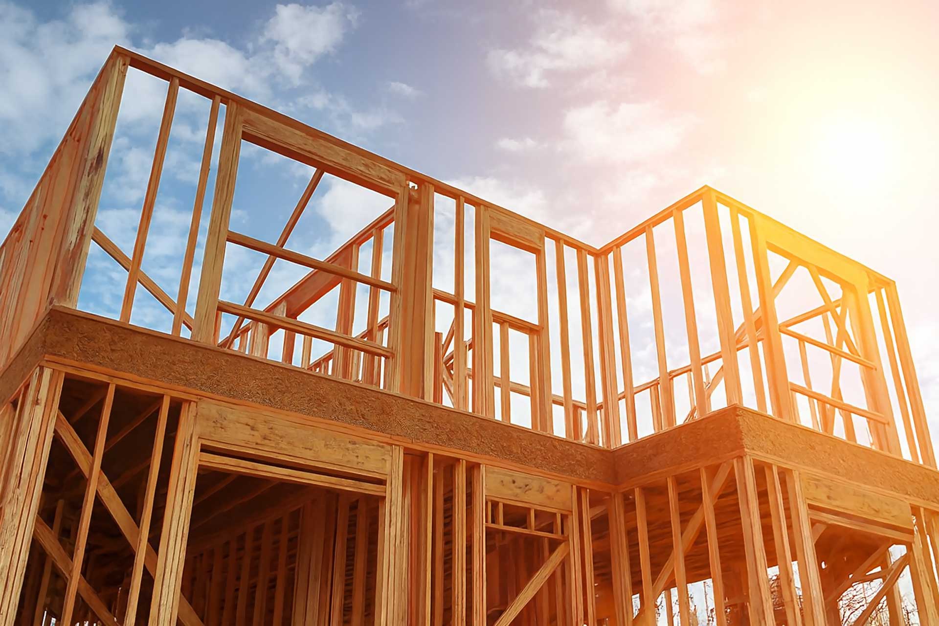 Two-storey timber house frame under construction against a bright sky