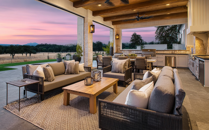 Covered outdoor living area with lounges, a timber coffee table and an outdoor kitchen at sunset