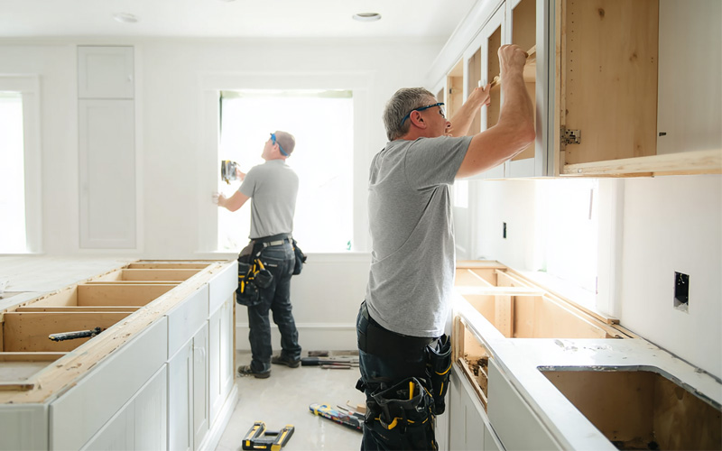 Two carpenters installing timber kitchen cabinets in a white kitchen