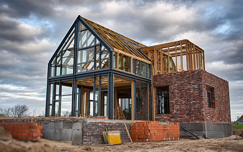 New house under construction with a steel and glass gable, timber framing and brick walls